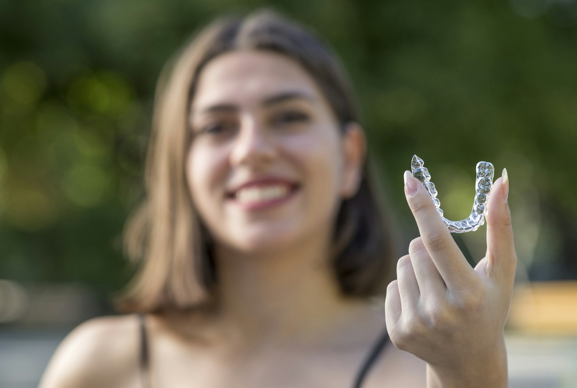 A woman holding up a clear Invisalign aligner, showcasing the benefits of Invisalign over traditional braces at Dalin Dental Associates.